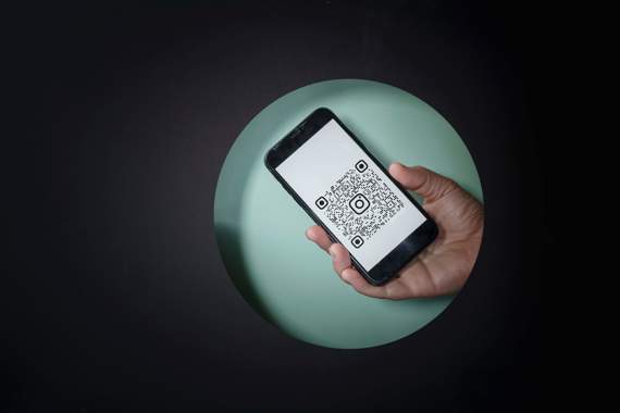 A hand holding cellphone. There is a QR code on the screen.